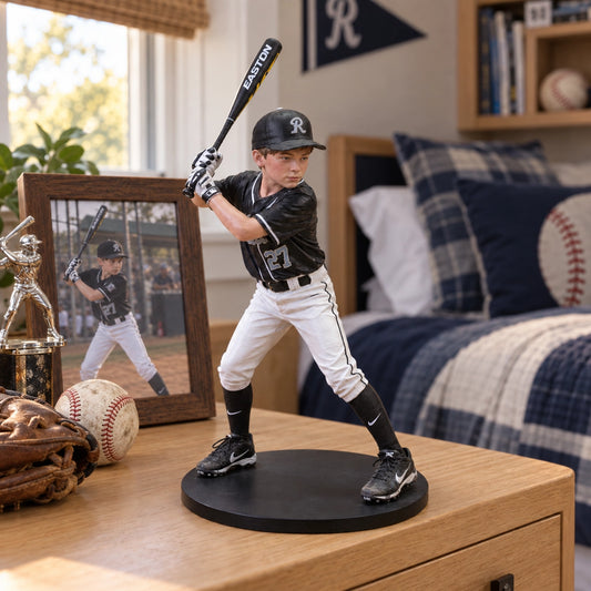 A baseball player figurine wearing a black and white uniform, posed as if batting, displayed on a wooden dresser in a bedroom setting next to a framed photo and baseball accessories.